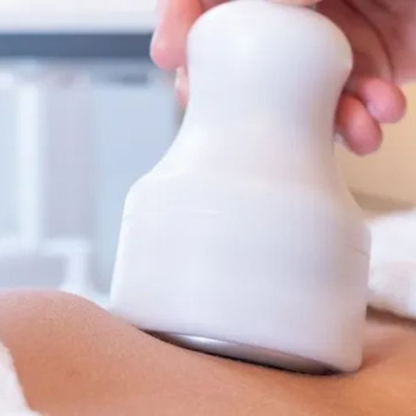 Esthetician using a specialized handheld massage wand for a body sculpting session on a client's abdomen at Bonfire Wellness