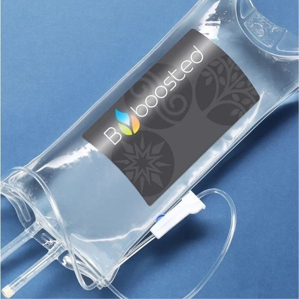 Clear IV therapy drip bag featuring the B boosted logo lying on a blue background.
