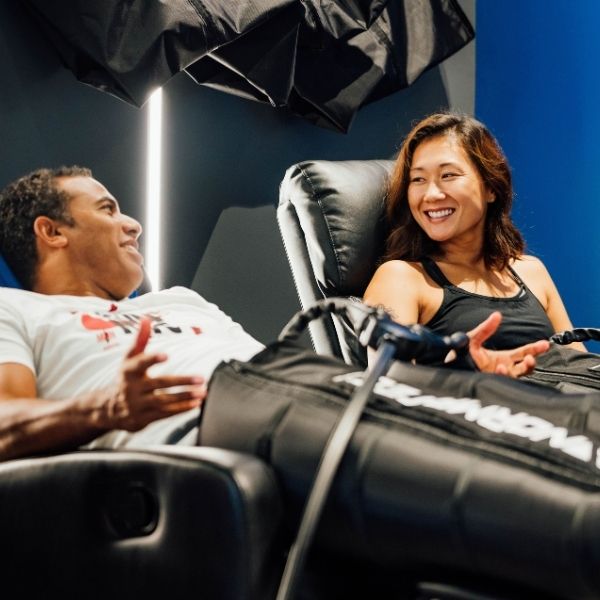 A man and a woman smiling and talking while enjoying a relaxing compression therapy at Bonfire Wellness.