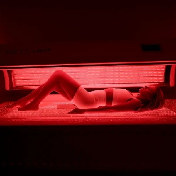 Woman lying inside a glowing red NEO Light Bed receiving full-body neo light bed therapy at Bonfire Wellness