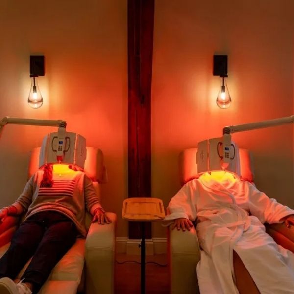 Two clients reclining in lounge chairs receiving targeted facial red light therapy under specialized glowing light panels at Bonfire Wellness
