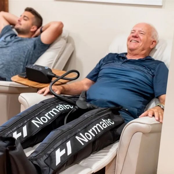 Two men relaxing in recovery chairs using compression therapy sleeves — Bonfire Wellness seniors specials