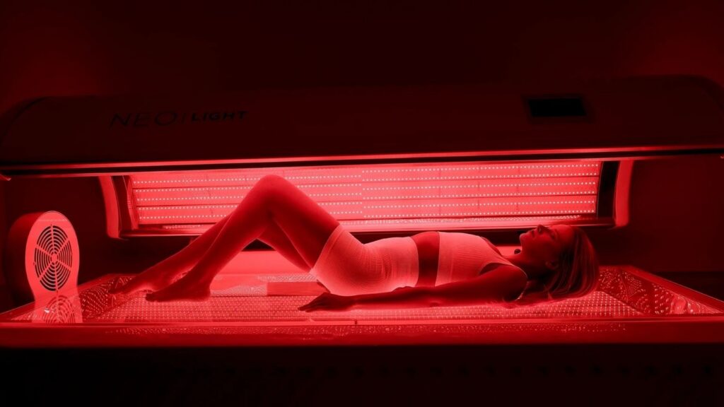 Woman lying inside a glowing red NEO Light Bed receiving full-body neo light bed therapy at Bonfire Wellness